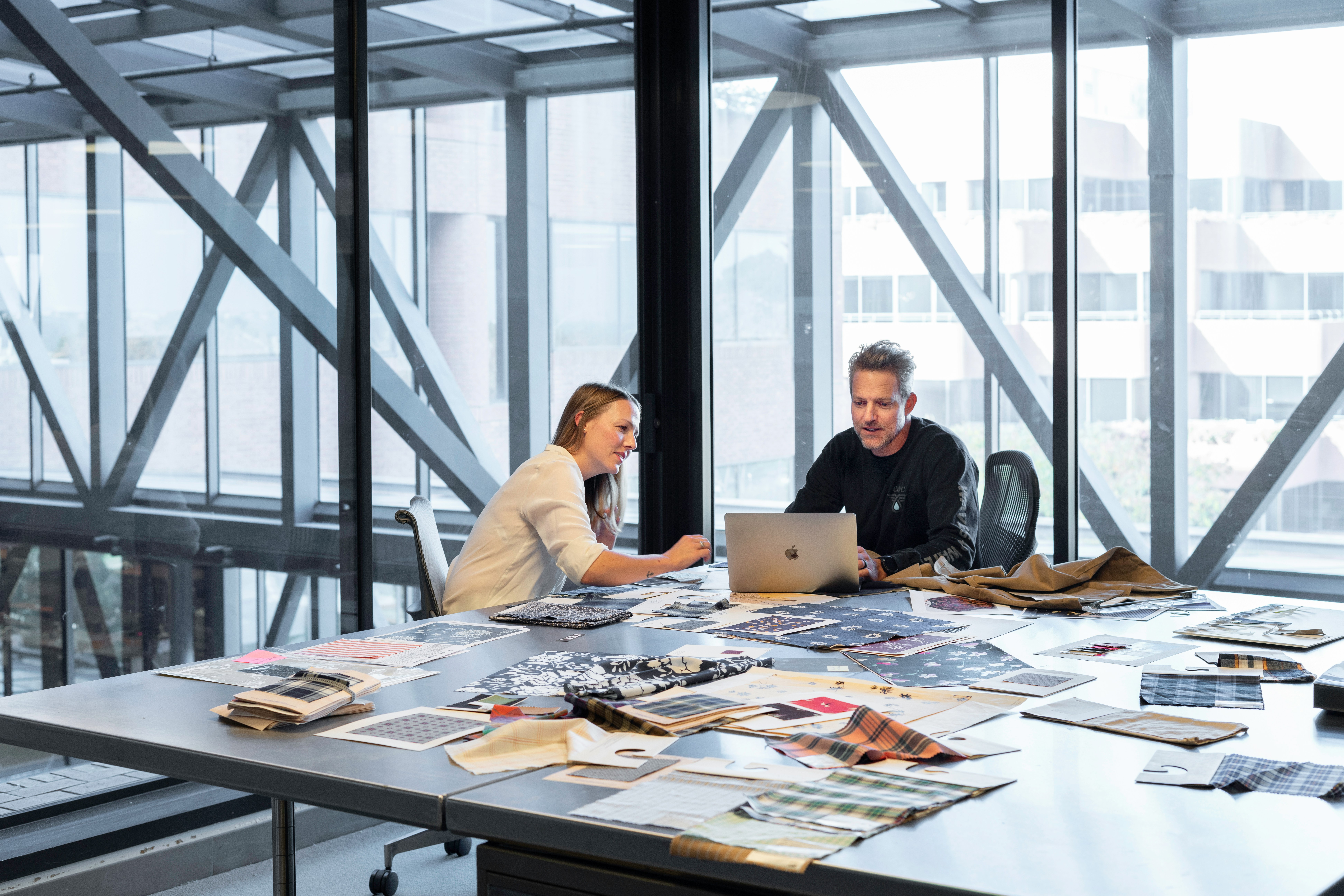Two people collaborating at a table with a laptop and materials